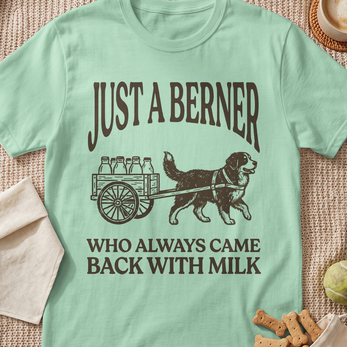 Light green t-shirt with brown text and illustration of a Bernese Mountain Dog pulling a milk cart.