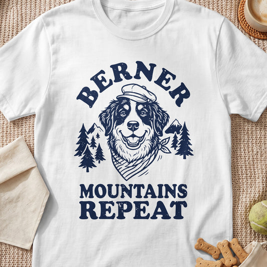 White t-shirt with navy graphic of a smiling dog wearing a hat and bandana, mountains, and trees, text "BERNER MOUNTAINS REPEAT".