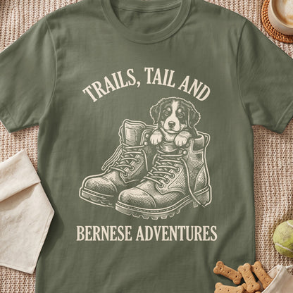 Bernese puppy in hiking boots with text "TRAILS, TAIL AND BERNESE ADVENTURES".