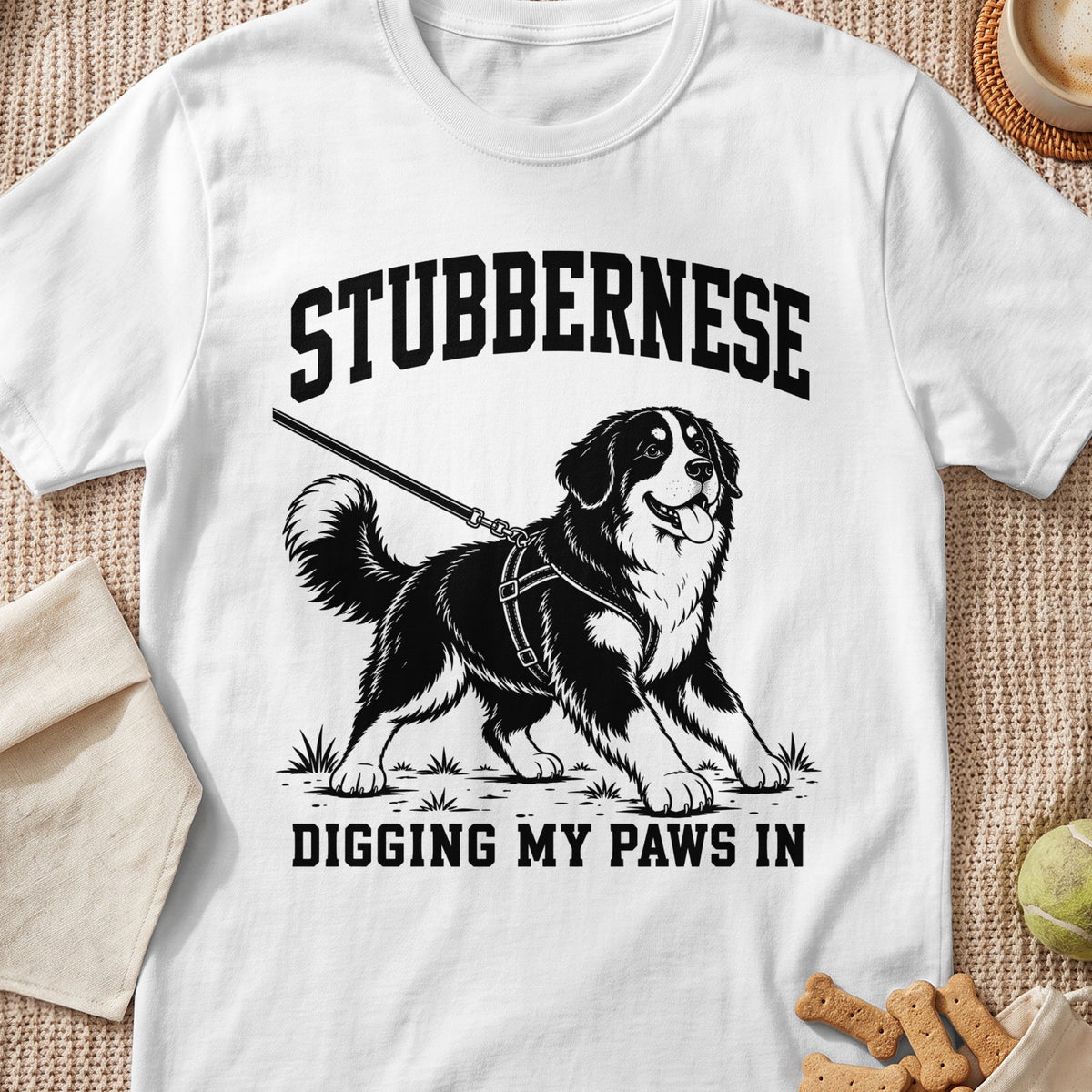 White t-shirt with black graphic of a Bernese Mountain Dog on a leash, text "STUBBERNESE DIGGING MY PAWS IN".