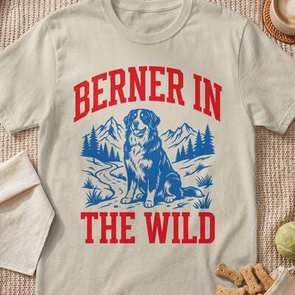 Bernese Mountain Dog sitting in a wild landscape with mountains and trees, text reads "BERNER IN THE WILD".