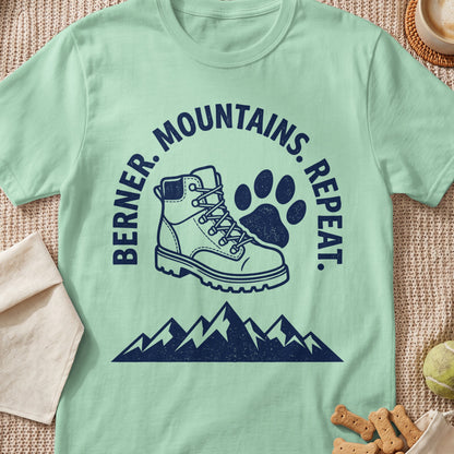 Mint green t-shirt with dark blue graphic of hiking boot, paw print, and mountains. Text reads "BERNER. MOUNTAINS. REPEAT."