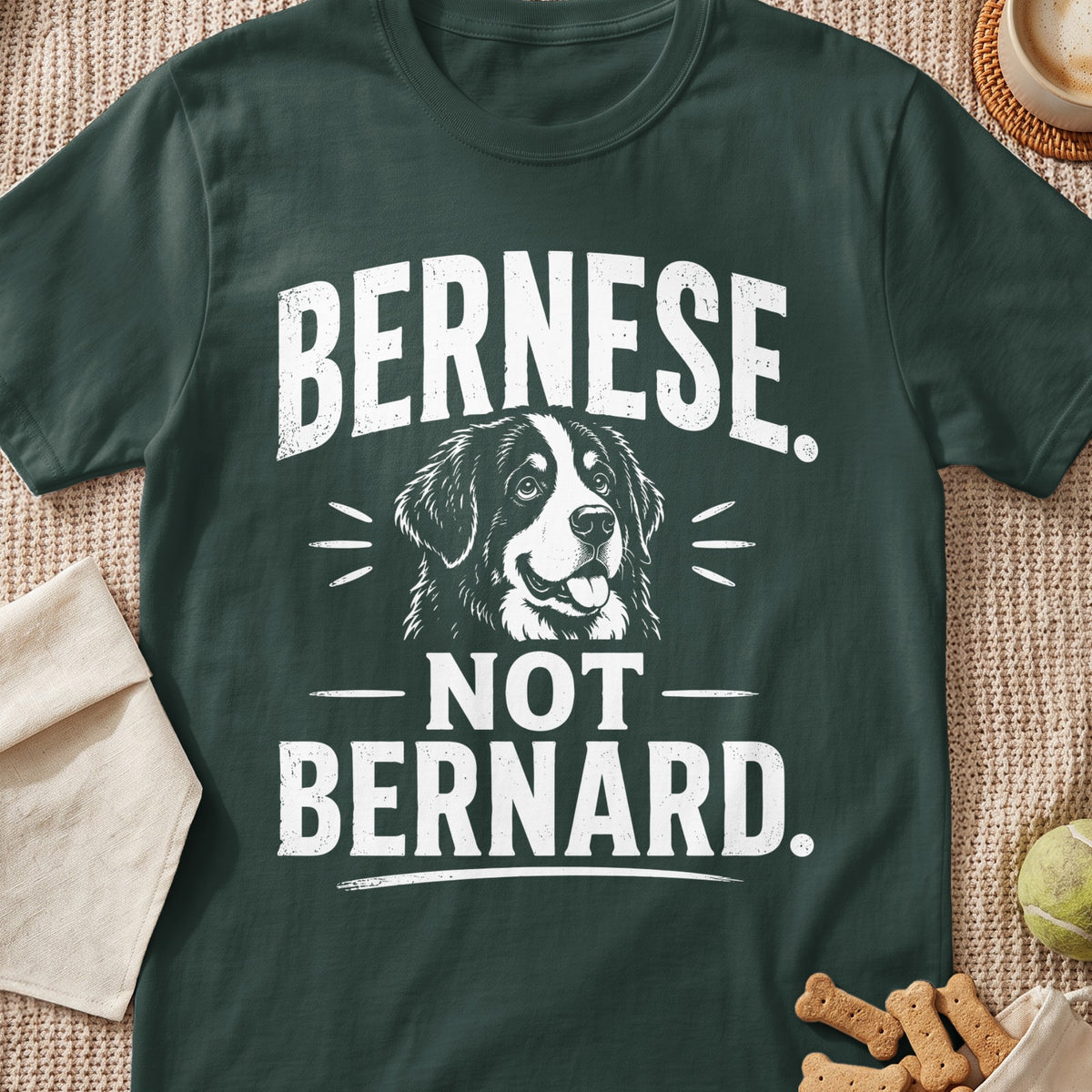 A dark green t-shirt featuring white text that reads "BERNESE. NOT BERNARD." with a dog illustration.