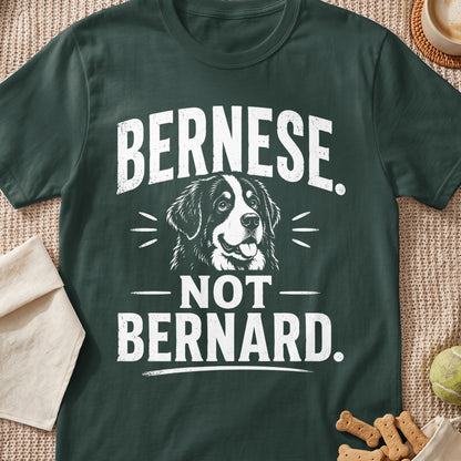 A dark green t-shirt featuring white text that reads "BERNESE. NOT BERNARD." with a dog illustration.