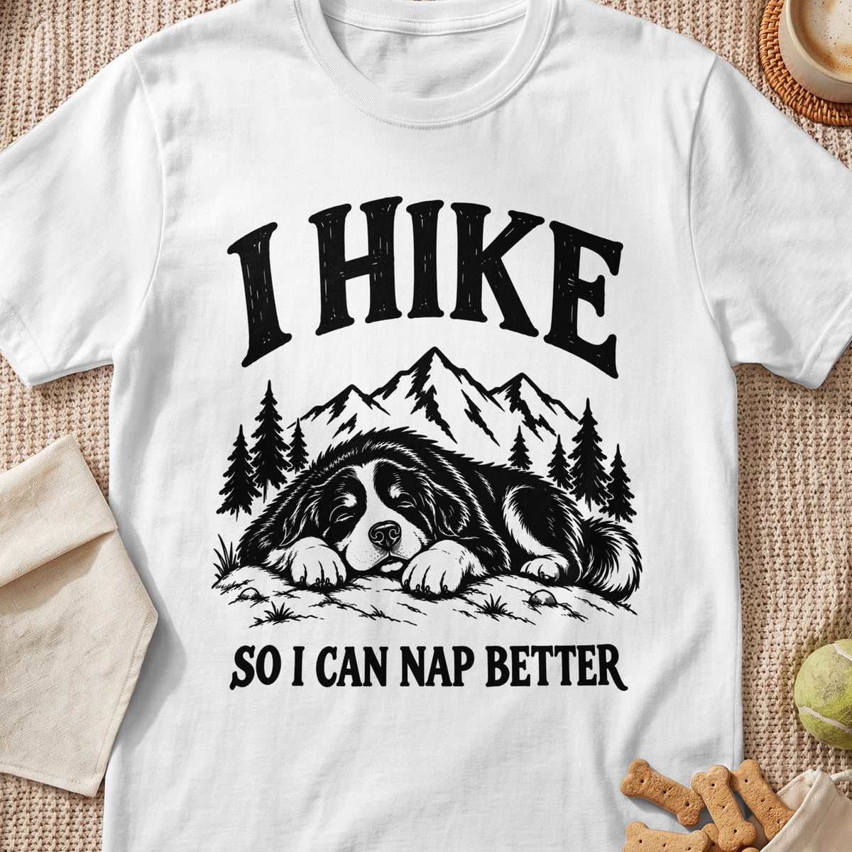 White t-shirt with black graphic of a Bernese Mountain Dog sleeping with mountains and trees, text "I HIKE SO I CAN NAP BETTER".