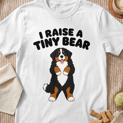 White t-shirt with black text "I RAISE A TINY BEAR" and cartoon Bernese Mountain Dog.