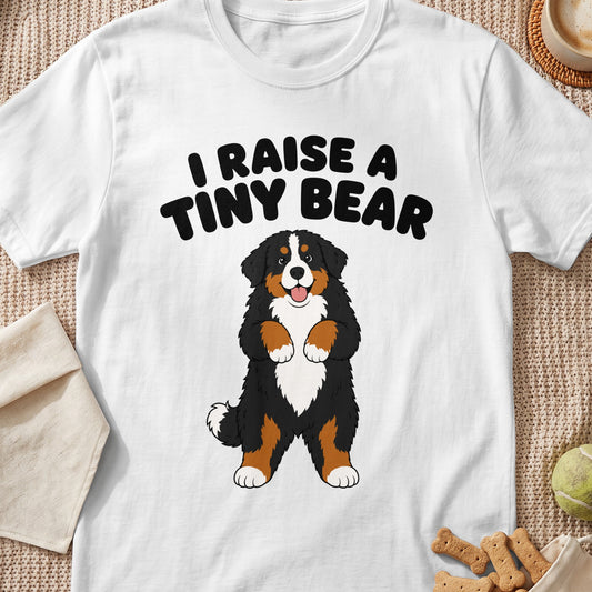 White t-shirt with black text "I RAISE A TINY BEAR" and cartoon Bernese Mountain Dog.