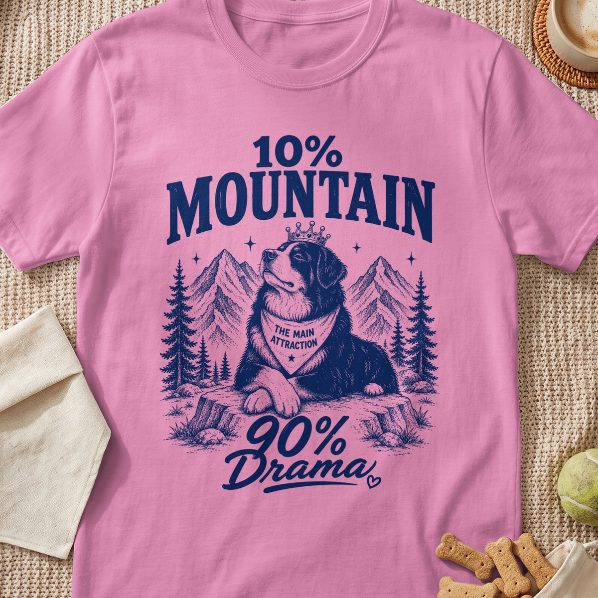 Pink t-shirt with a blue graphic of a Bernese Mountain Dog wearing a crown and bandana amidst mountains.