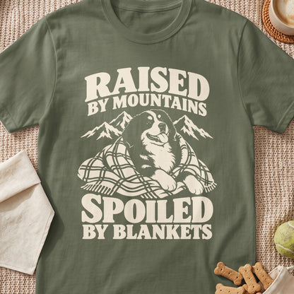Olive green t-shirt with dog, mountains, and text "Raised by Mountains, Spoiled by Blankets."