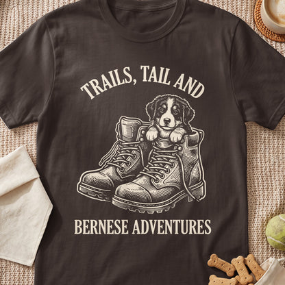 Bernese puppy in hiking boots with text "Trails, Tail and Bernese Adventures."