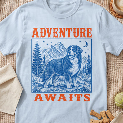 Light blue t-shirt with blue ink drawing of a Bernese Mountain Dog with mountains and "ADVENTURE AWAITS" text.