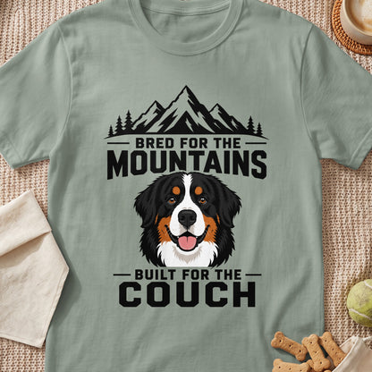 Sage green t-shirt featuring a Bernese Mountain Dog illustration with mountains and text reading Bred for the Mountains, Built for the Couch.