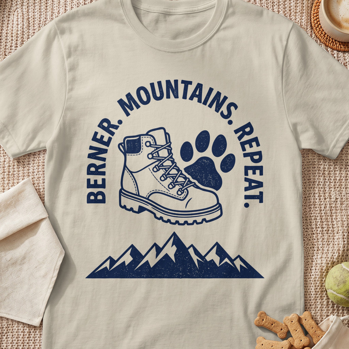 Cream t-shirt with navy graphic of hiking boot, paw print, and mountains with text: Berner. Mountains. Repeat.
