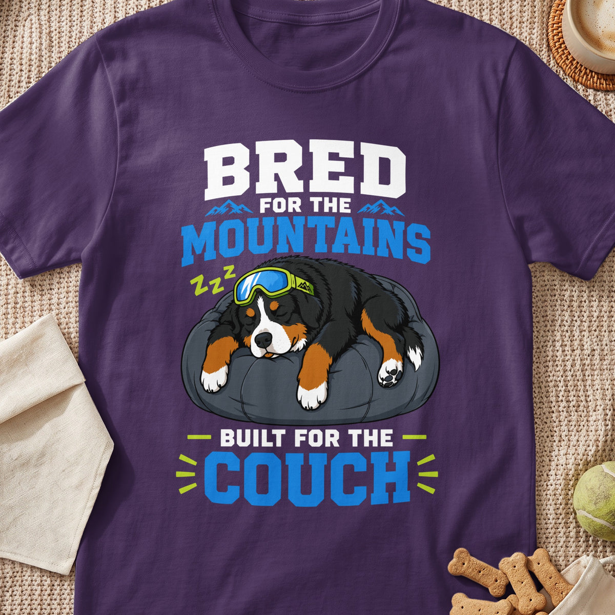 Bernese Mountain Dog with goggles sleeps on a bed, text says "Bred for the mountains, built for the couch."