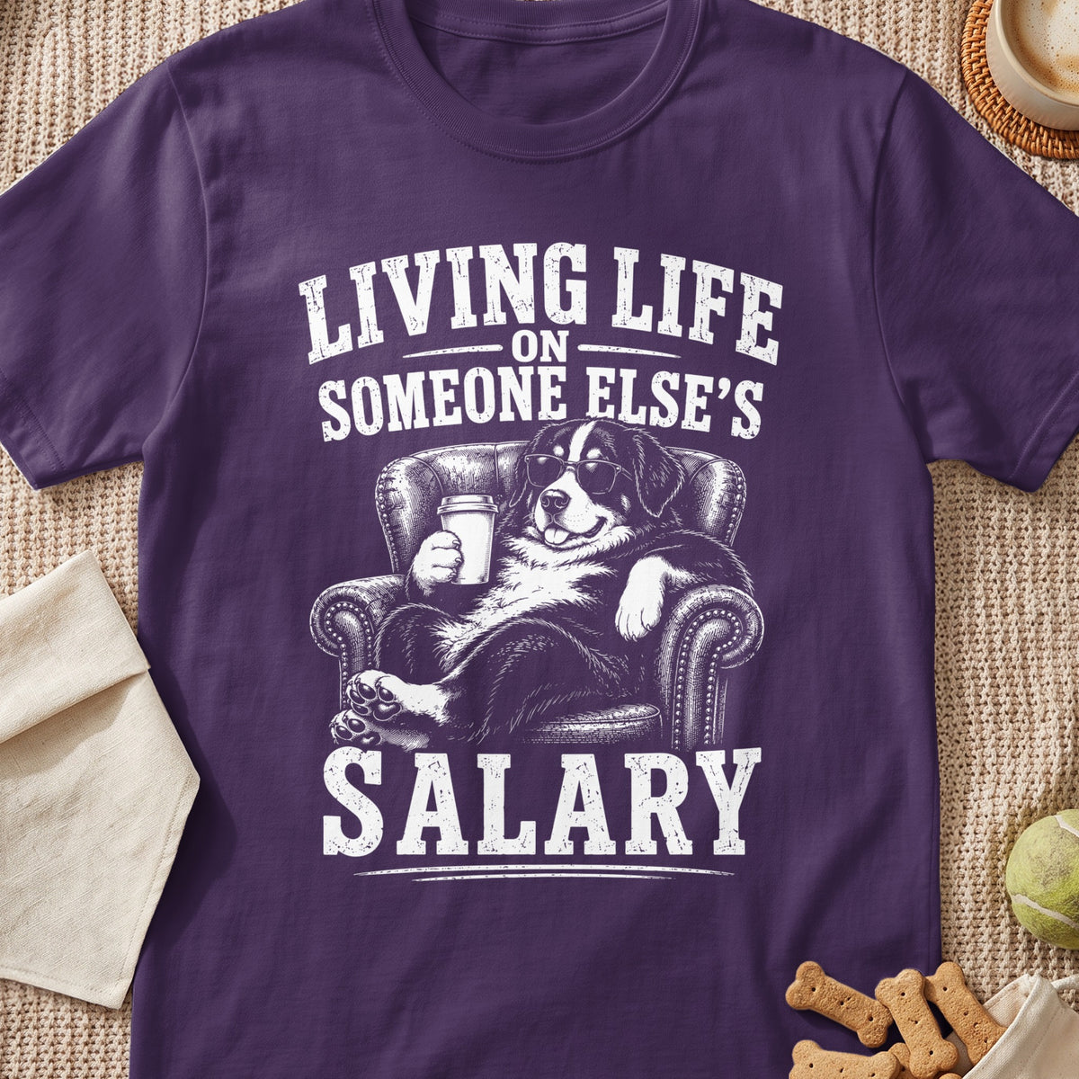 Bernese Mountain Dog wearing sunglasses, holding coffee and sitting on a couch, text reads "Living Life On Someone Else's Salary".