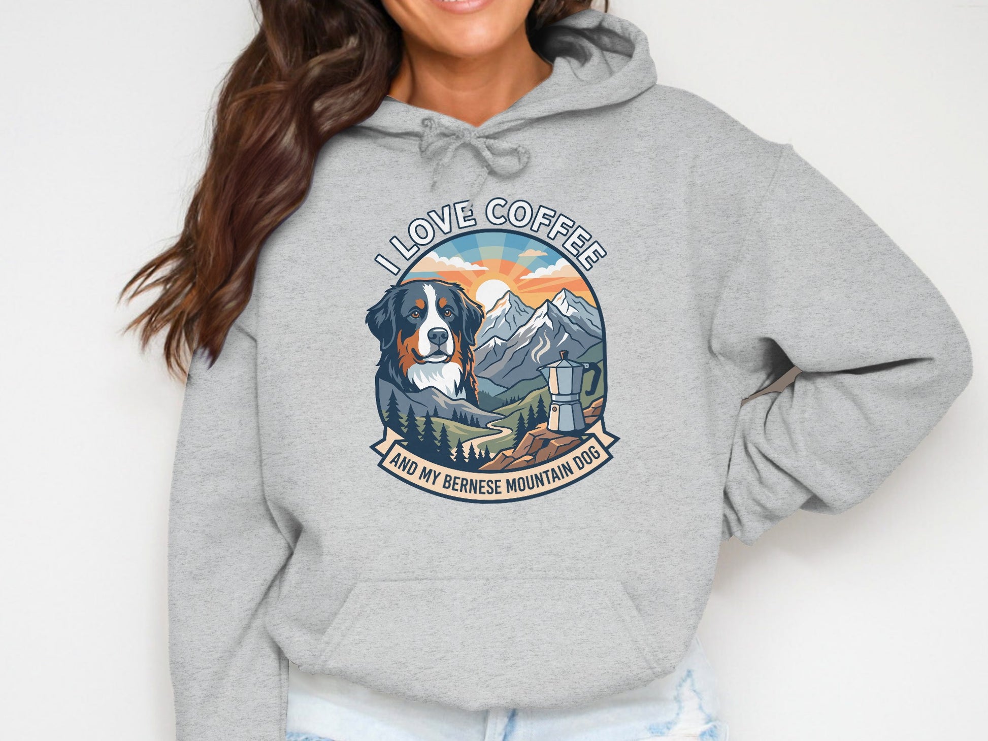 Bernese Mountain Dog and coffee graphic on a gray hoodie, surrounded by mountains and sunset.
