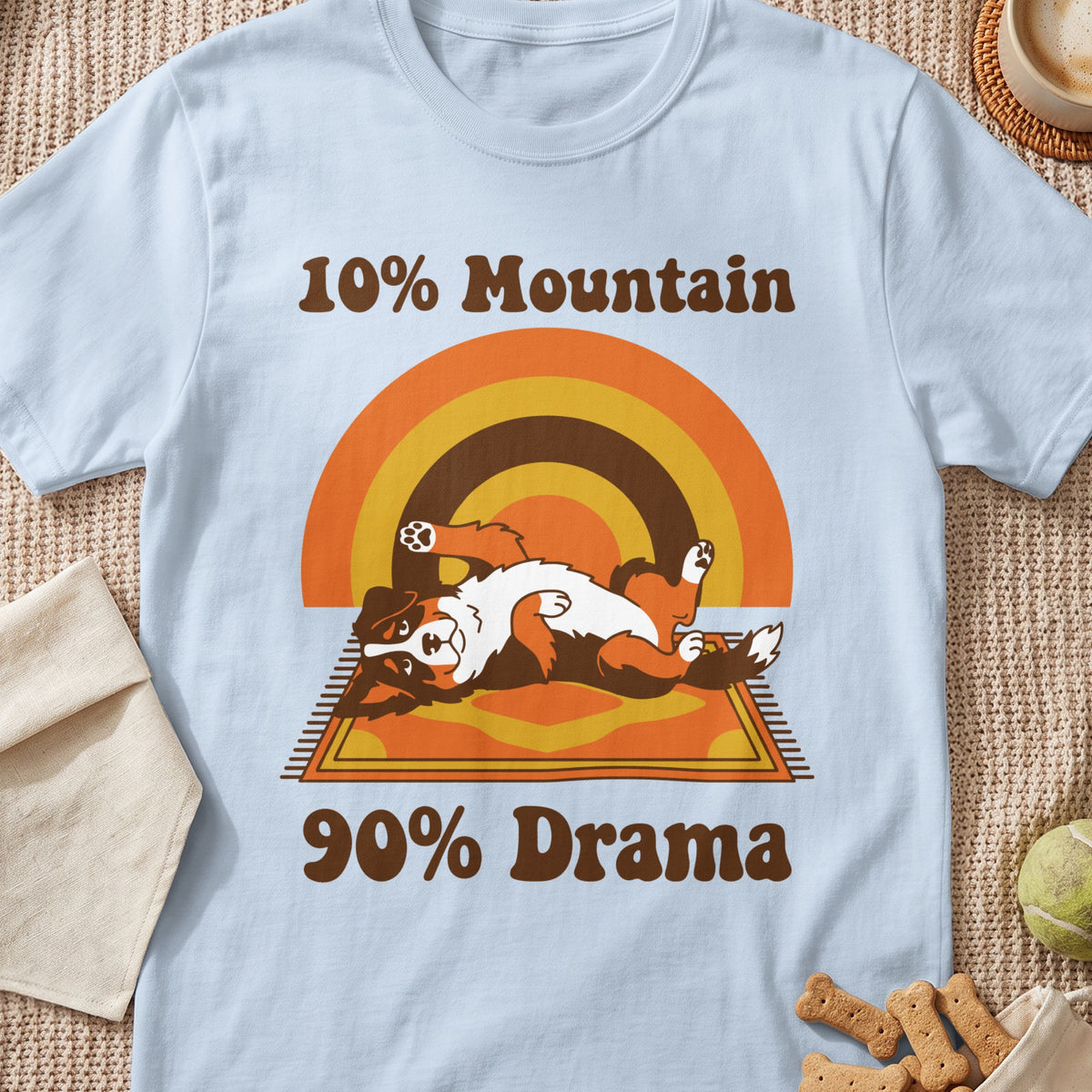 A light blue t-shirt featuring an illustration of an Australian Shepherd lying on its back with the text 10% Mountain 90% Drama.