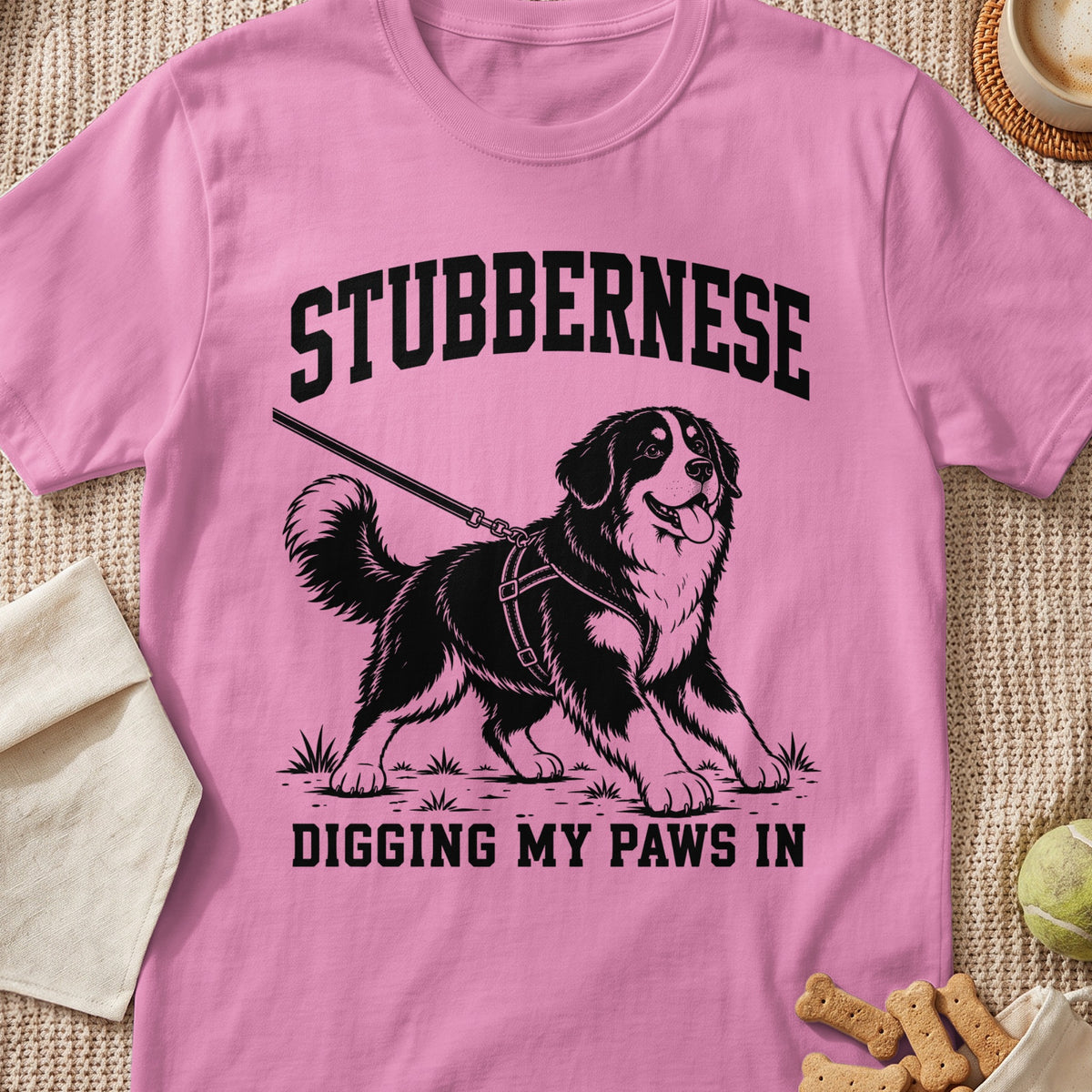 Pink t-shirt with black graphic of a Bernese Mountain Dog wearing a harness and leash, and text "STUBBERNESE DIGGING MY PAWS IN".