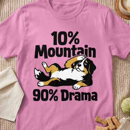 A pink short-sleeved t-shirt featuring a cartoon Bernese Mountain Dog lying down with black text that reads 10% Mountain 90% Drama.