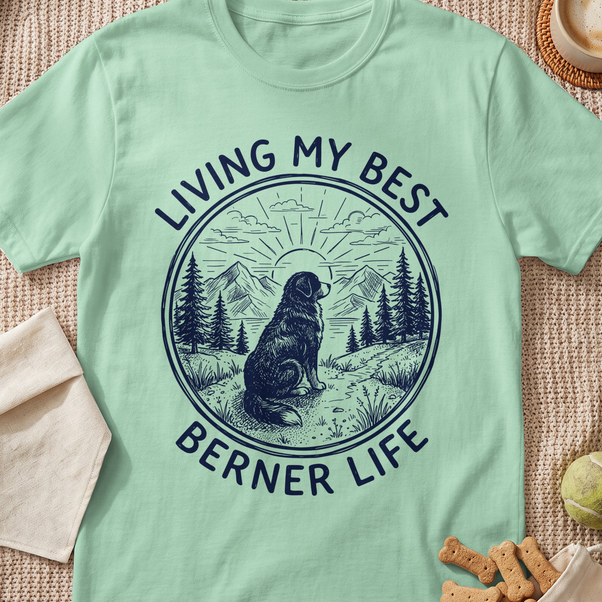 Light green t-shirt with a round graphic of a dog, mountains, and trees, featuring text reading "Living My Best Berner Life".