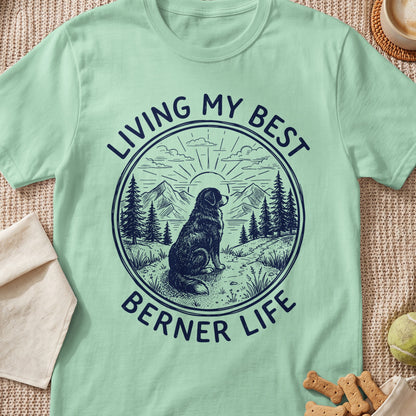 Light green t-shirt with a round graphic of a dog, mountains, and trees, featuring text reading "Living My Best Berner Life".
