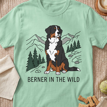 Bernese Mountain Dog sitting in a wild landscape with trees and mountains. Text says "BERNER IN THE WILD".