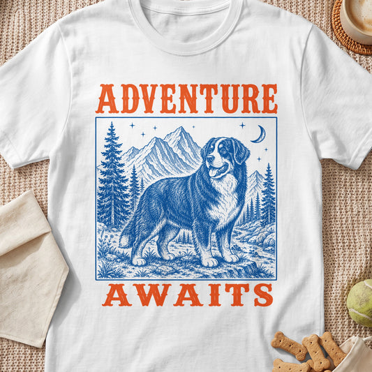White t-shirt with blue and orange graphic of a Bernese Mountain Dog in a mountainous landscape with text "ADVENTURE AWAITS".