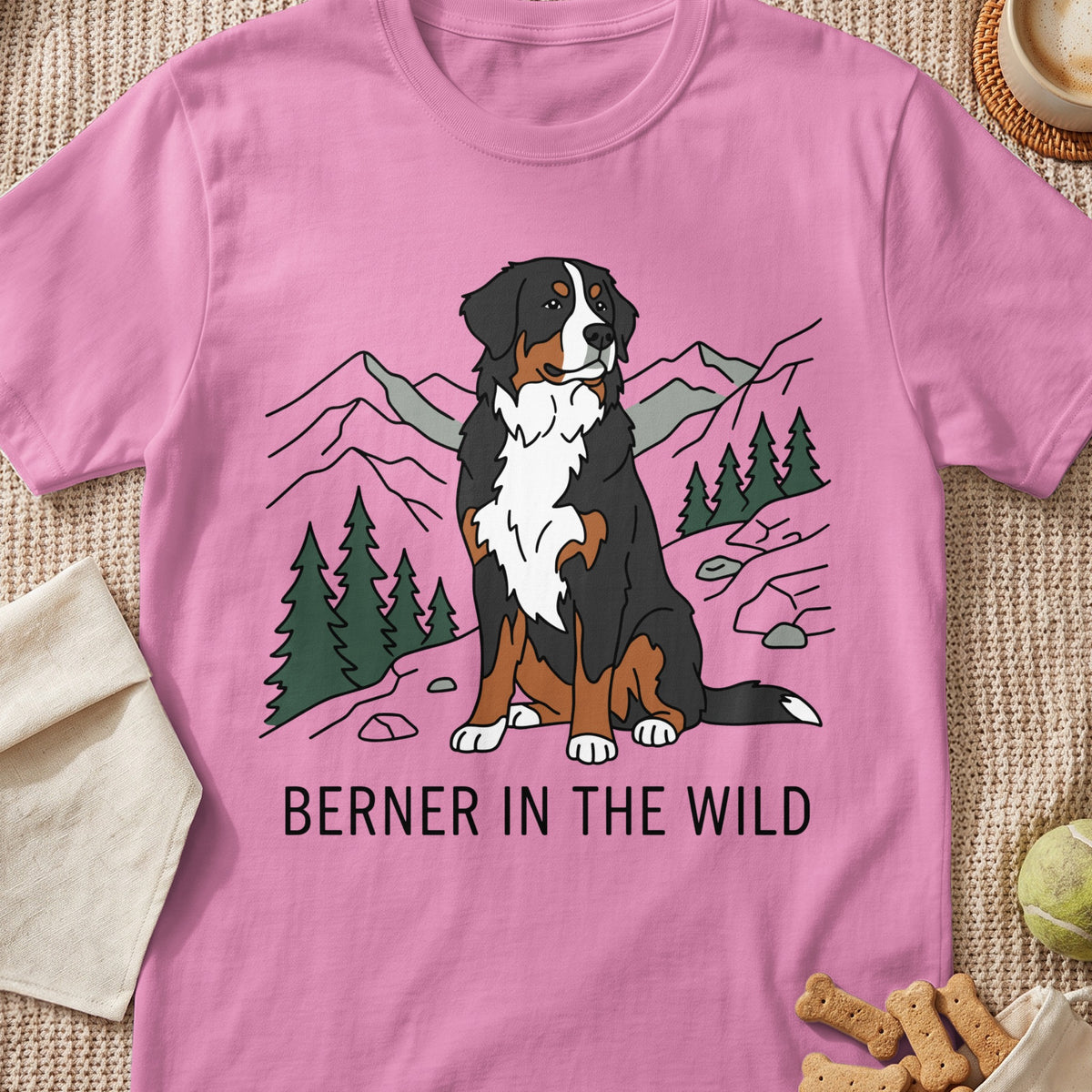 Pink t-shirt with a drawing of a Bernese Mountain Dog sitting in a mountain landscape, text reads "BERNER IN THE WILD".