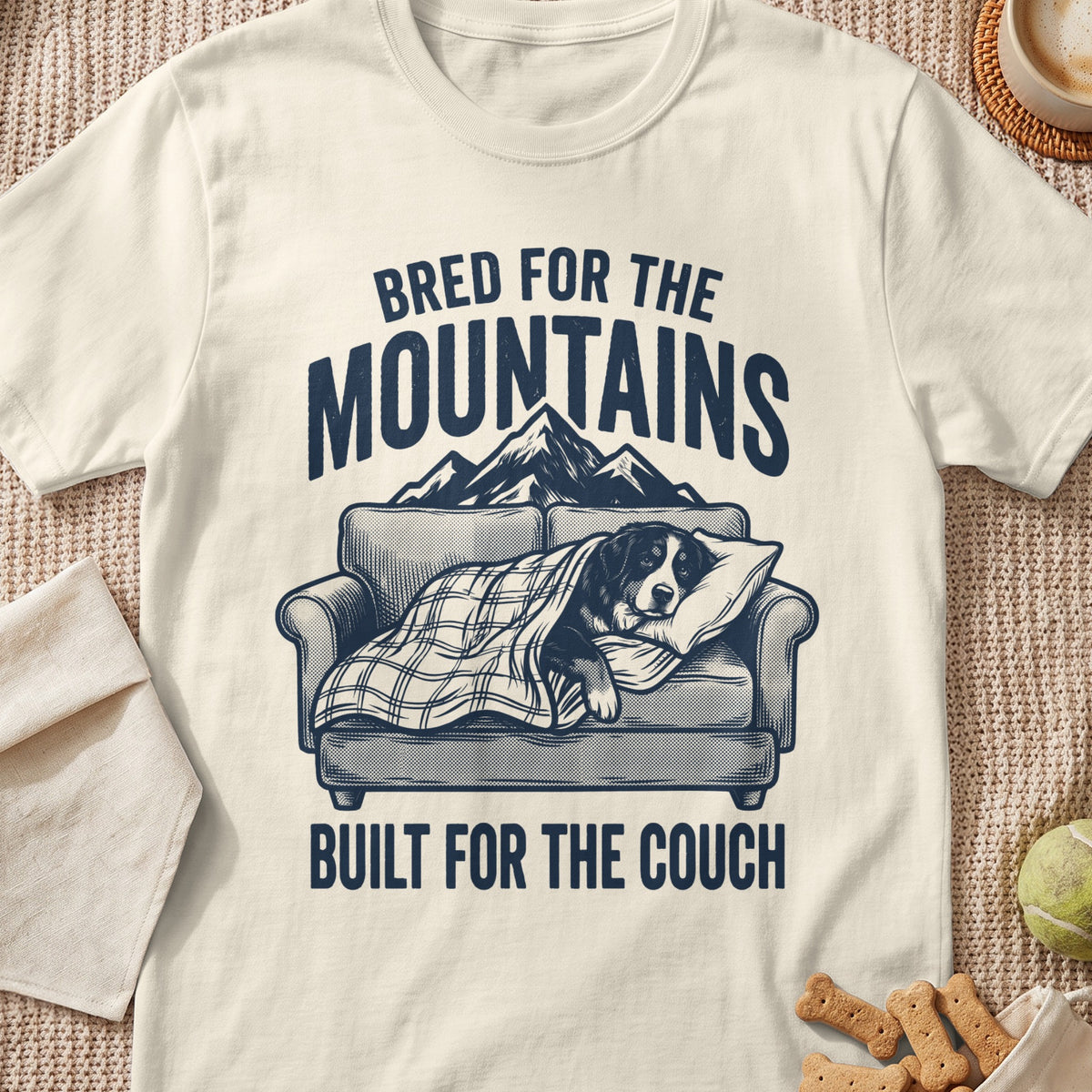 Dog on couch under blanket with text "Bred for the Mountains, Built for the Couch."