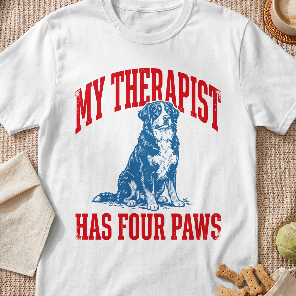 White t-shirt with red text "MY THERAPIST HAS FOUR PAWS" and a blue dog illustration.