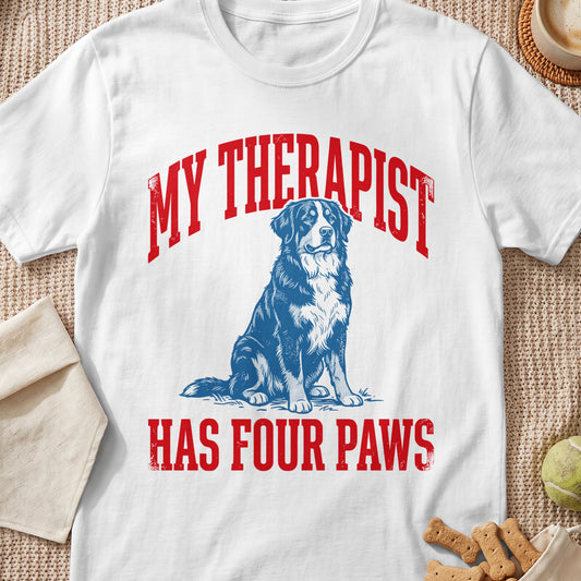 White t-shirt with red text "MY THERAPIST HAS FOUR PAWS" and a blue dog illustration.