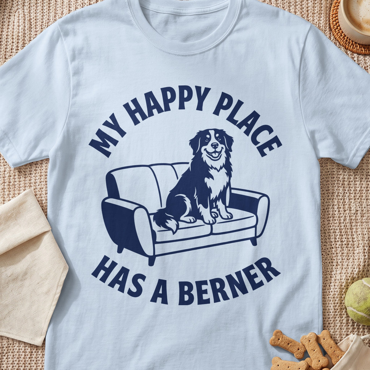 Light blue t-shirt with navy graphic of happy Bernese mountain dog on couch, text "MY HAPPY PLACE HAS A BERNER".