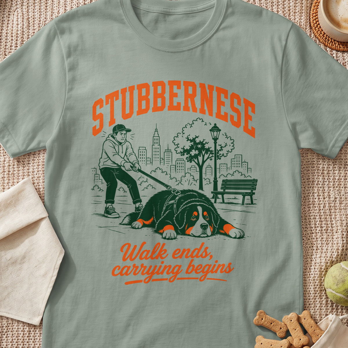 T-shirt graphic: Stubborn Bernese dog lying down, person pulling leash, city background, text "Walk ends, carrying begins".