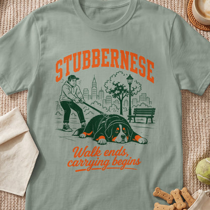 T-shirt graphic: Stubborn Bernese dog lying down, person pulling leash, city background, text "Walk ends, carrying begins".