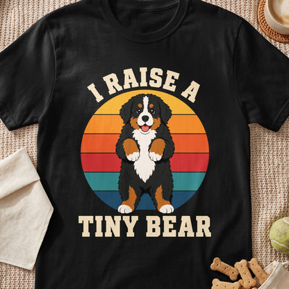 Bernese Mountain Dog with text "I RAISE A TINY BEAR" on a sunset background.