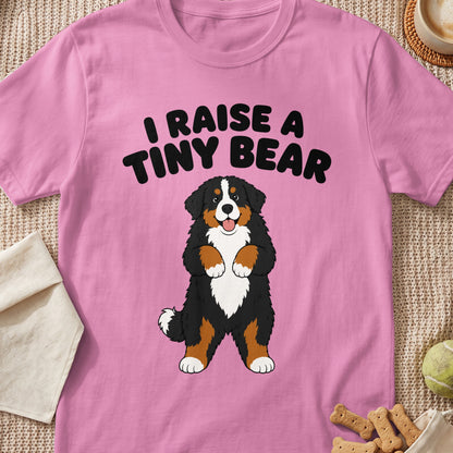 Pink t-shirt with black text "I RAISE A TINY BEAR" above a cartoon Bernese Mountain Dog.