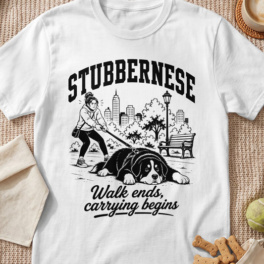 White t-shirt with "STUBBERNESE" text above a drawing of a woman struggling to walk a large, reclining dog.
