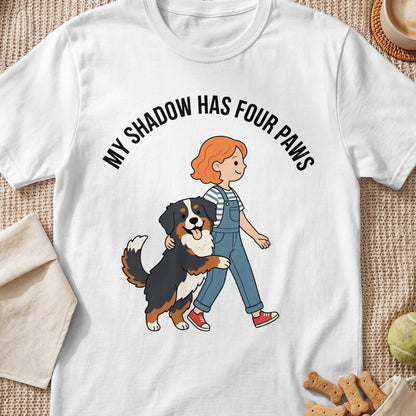White t-shirt with text "MY SHADOW HAS FOUR PAWS" and cartoon of girl walking dog.